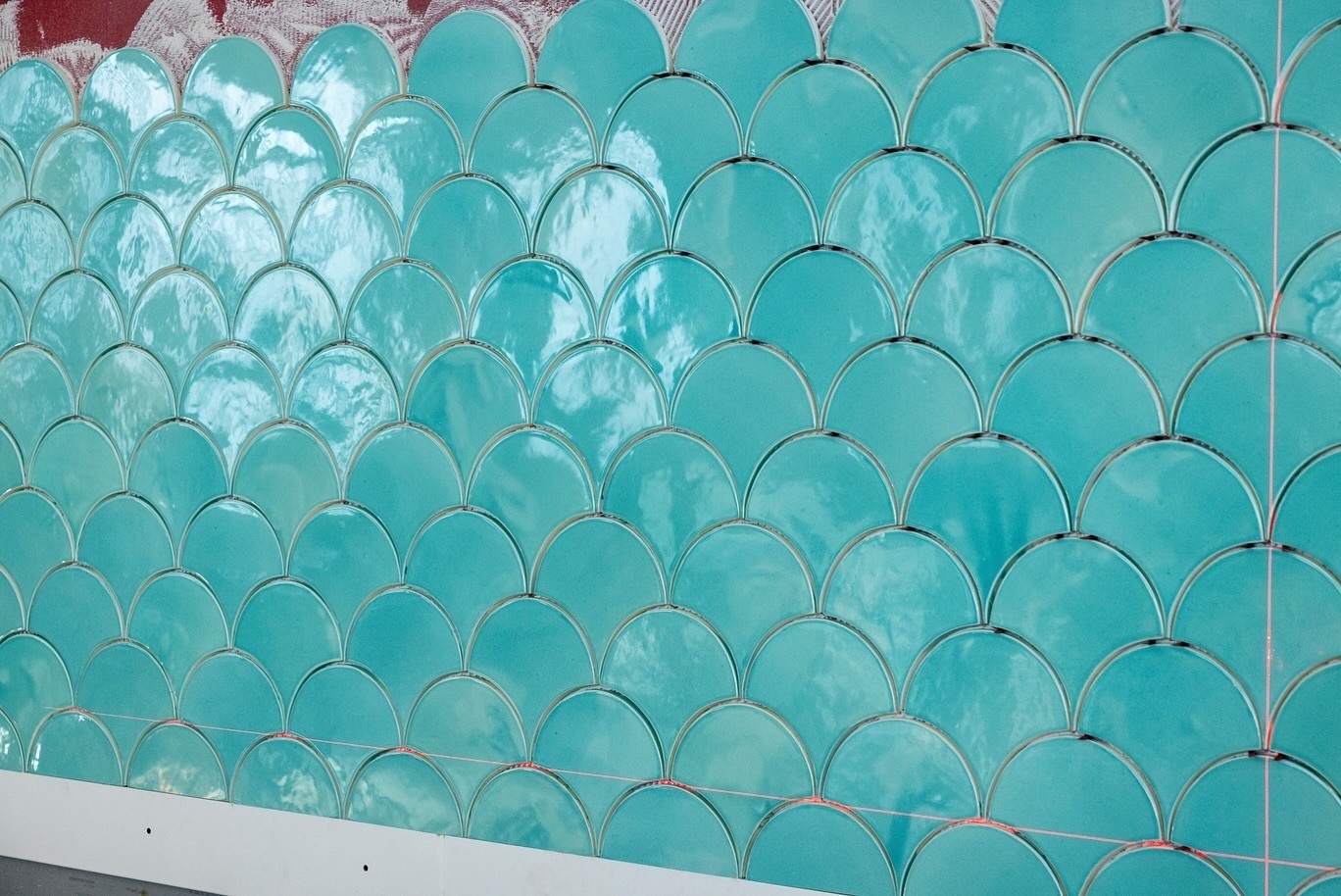 A wall is covered with turquoise, scalloped tiles arranged in a pattern.