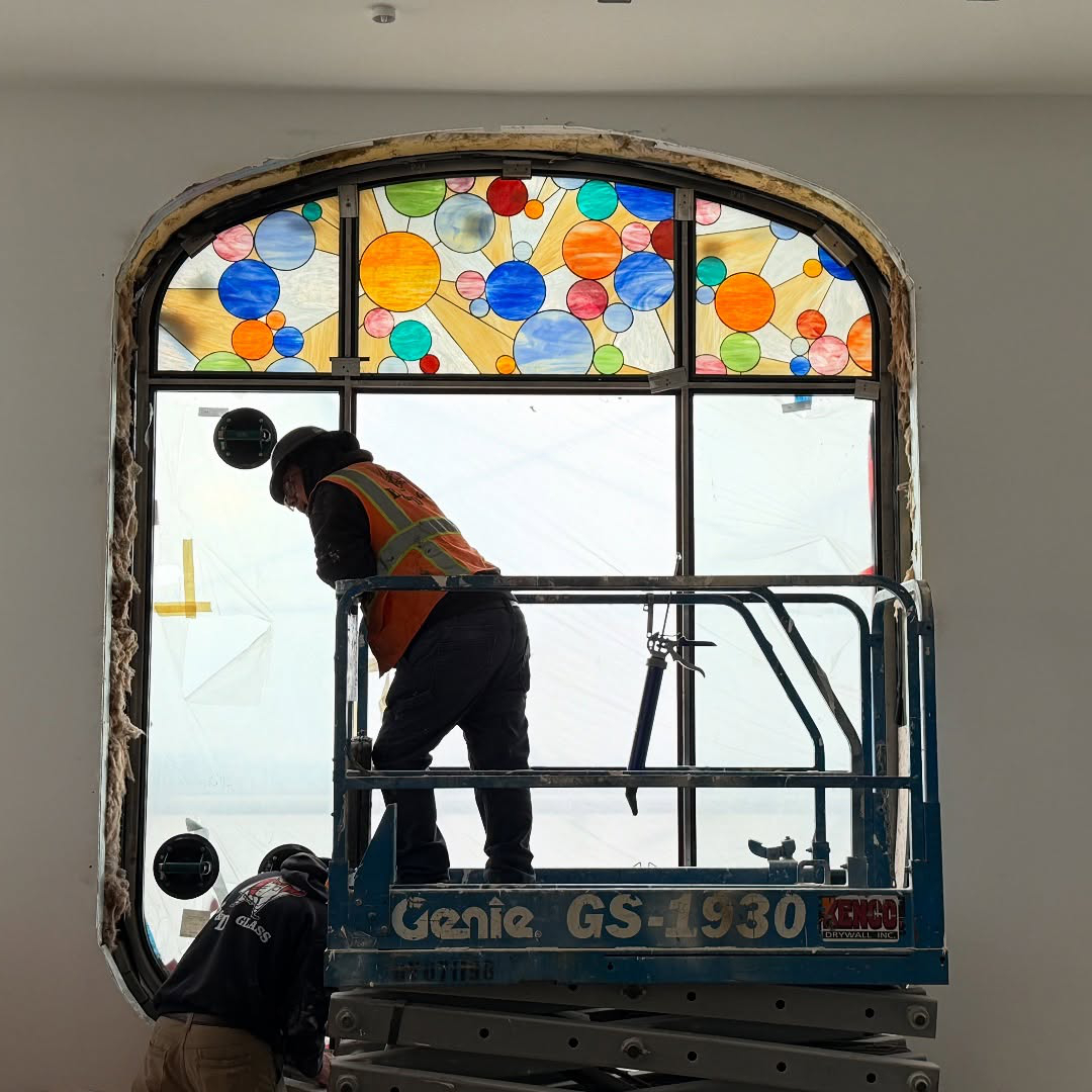 A worker is on a scissor lift installing a colorful stained glass window.