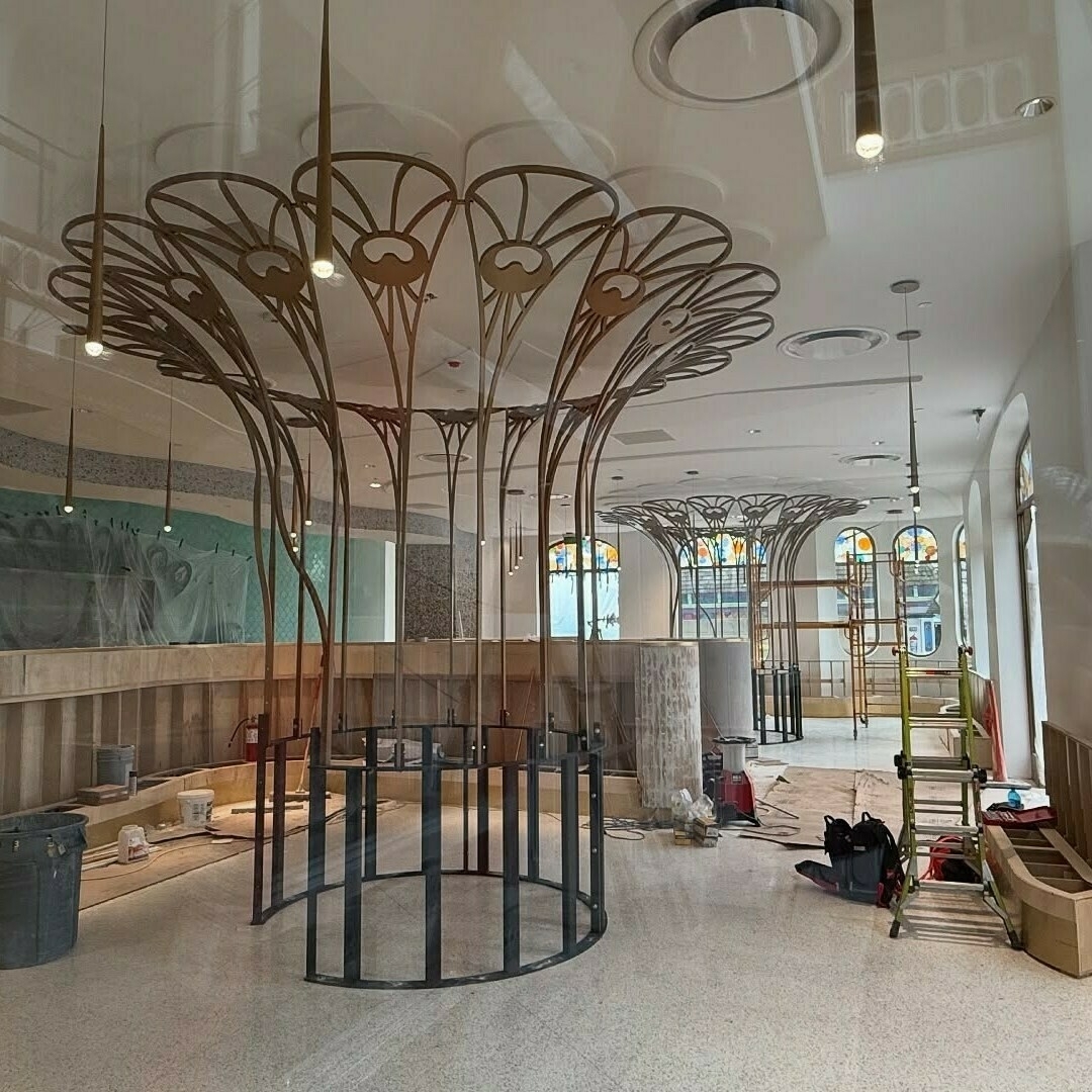 A partly constructed interior features ornate metal tree-like structures, building materials, and scattered tools.