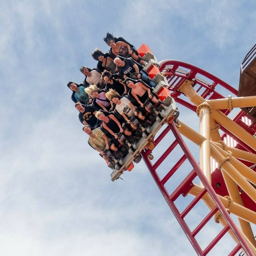 A group of people are riding a roller coaster, descending a steep drop while expressing excitement and thrill.