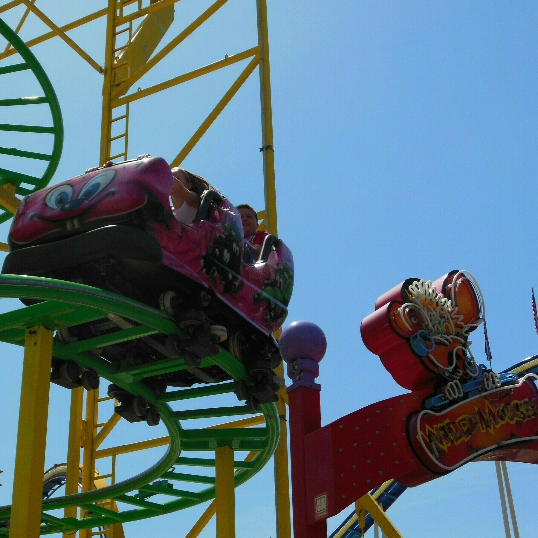 A picture of the Wild Mouse roller coaster. The image frames the shot with one of the cars on a turn near the entrance sign.