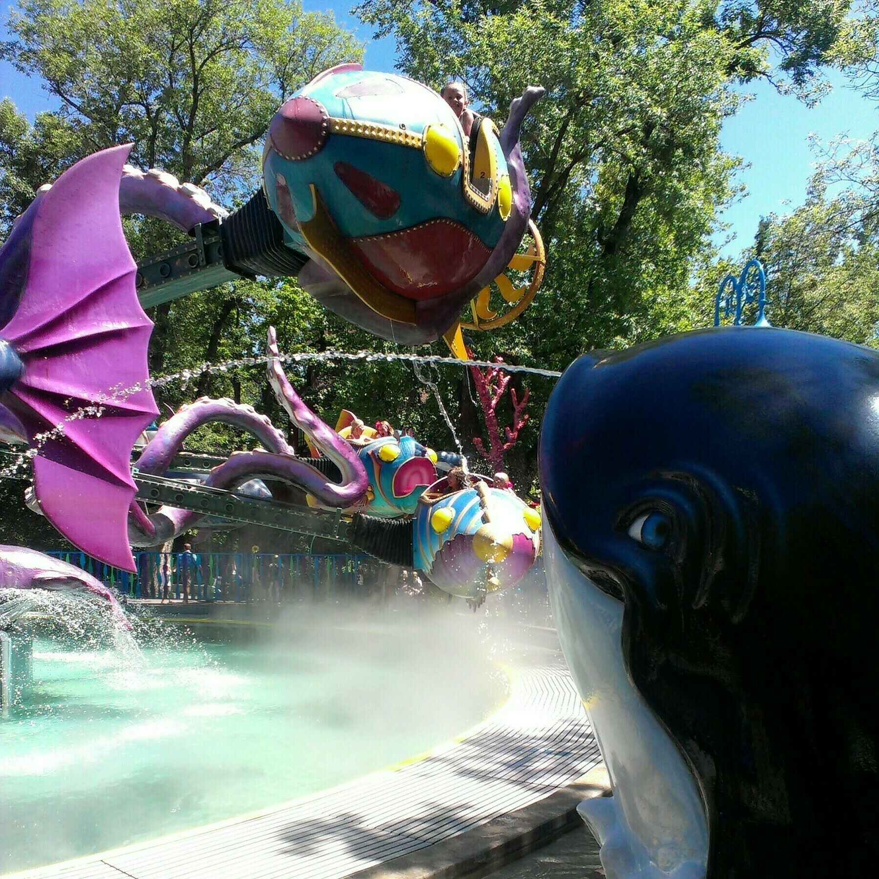 OdySea at Lagoon Amusement Park. The ride is in motion with the ride vehicles in the air going around. The photo is taken from next to one of the aquatic animals that spit water at passing vehicles.