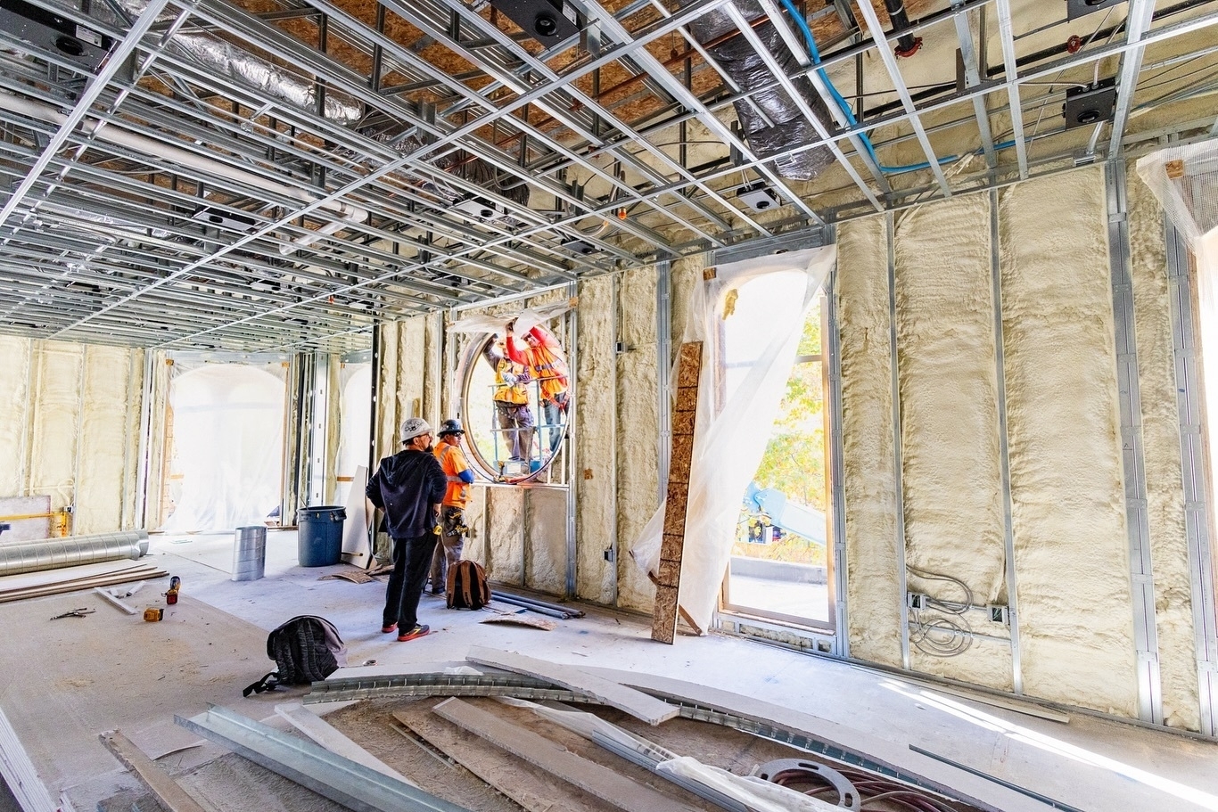 Construction workers installing framing for a new window. The inside shows exposed metal framing and unfinished walls.