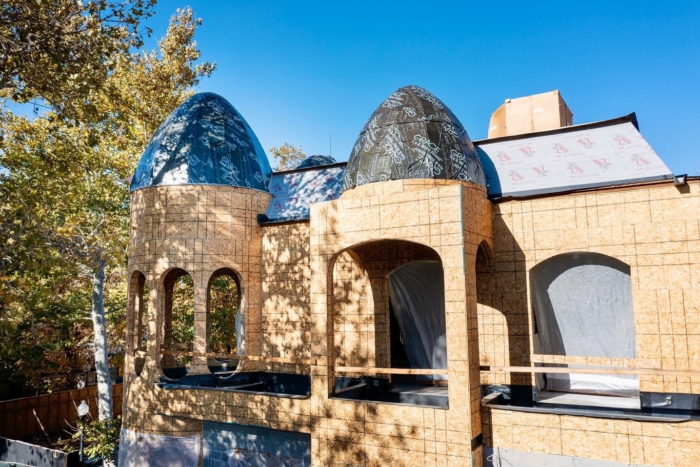 A partially constructed building features arched openings and distinctive dome-shaped roofs against a clear blue sky.