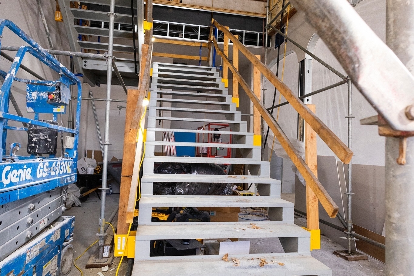 A construction site features a partly constructed staircase surrounded by scaffolding and various building materials.