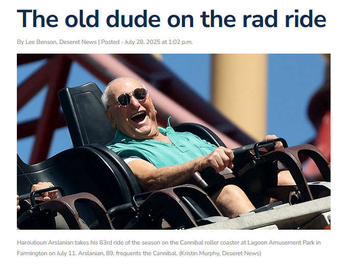 A man joyfully rides a roller coaster with his hands raised and sunglasses on.