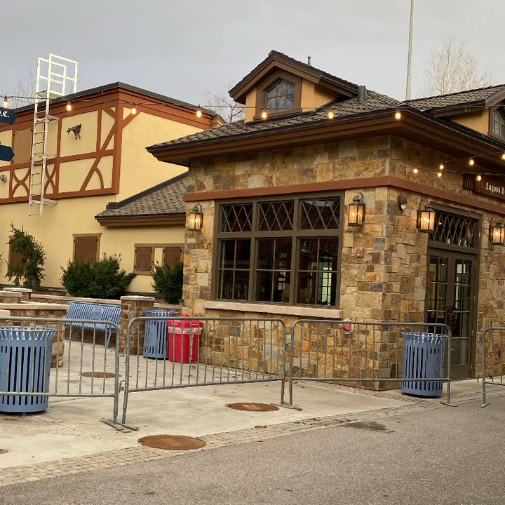 A restaurant or building with stone walls and wooden beams is surrounded by metal barricades and trash bins.