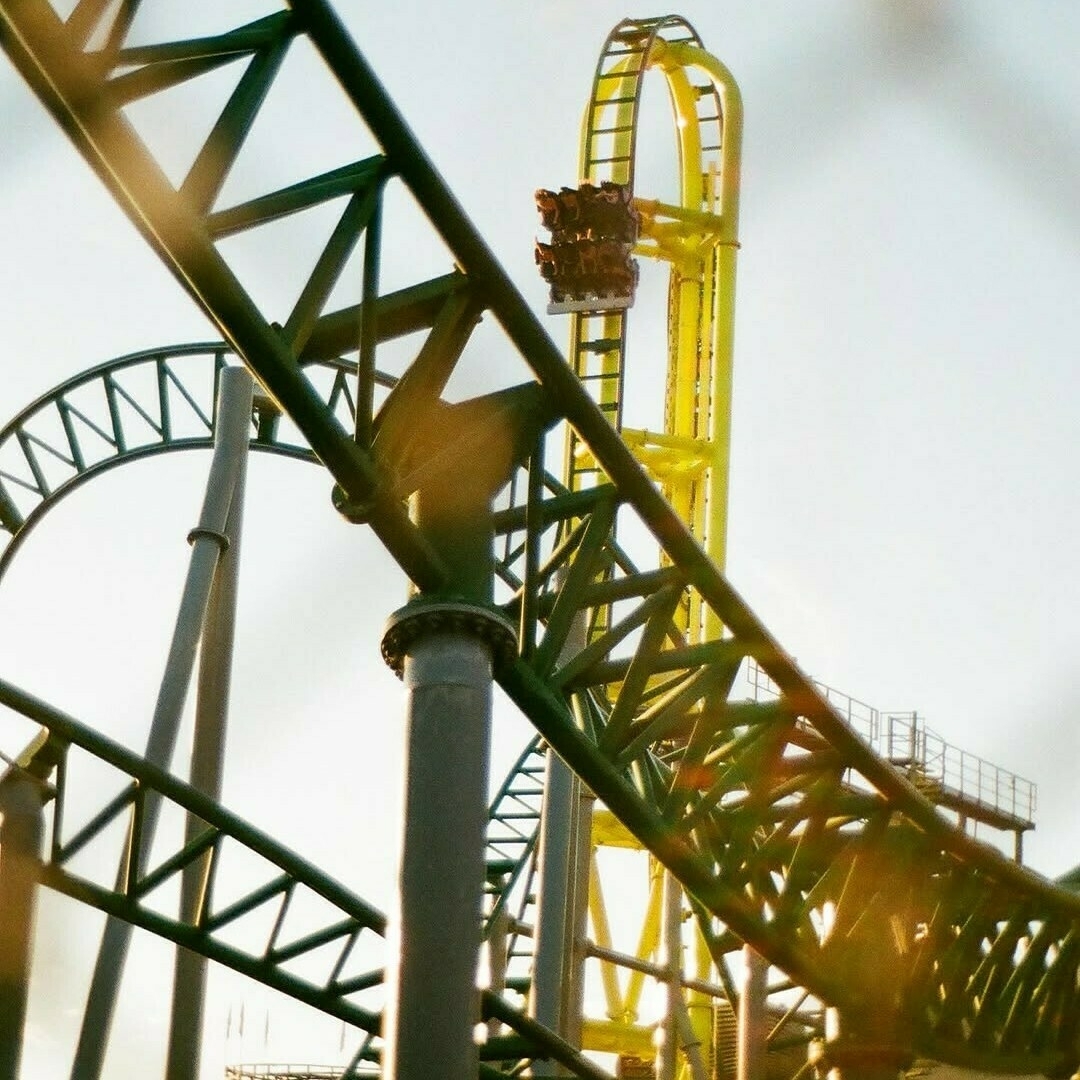 A view of Wicked with the part of the track in front of the vertical tower. A car is coming down the vertical drop. Image looks like it was taken on film with some sun glares.