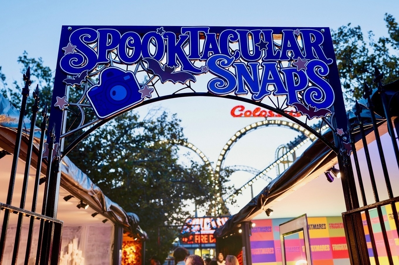A decorated archway with the words "Spooktacular Snaps" leads to a festive area in an amusement park.
